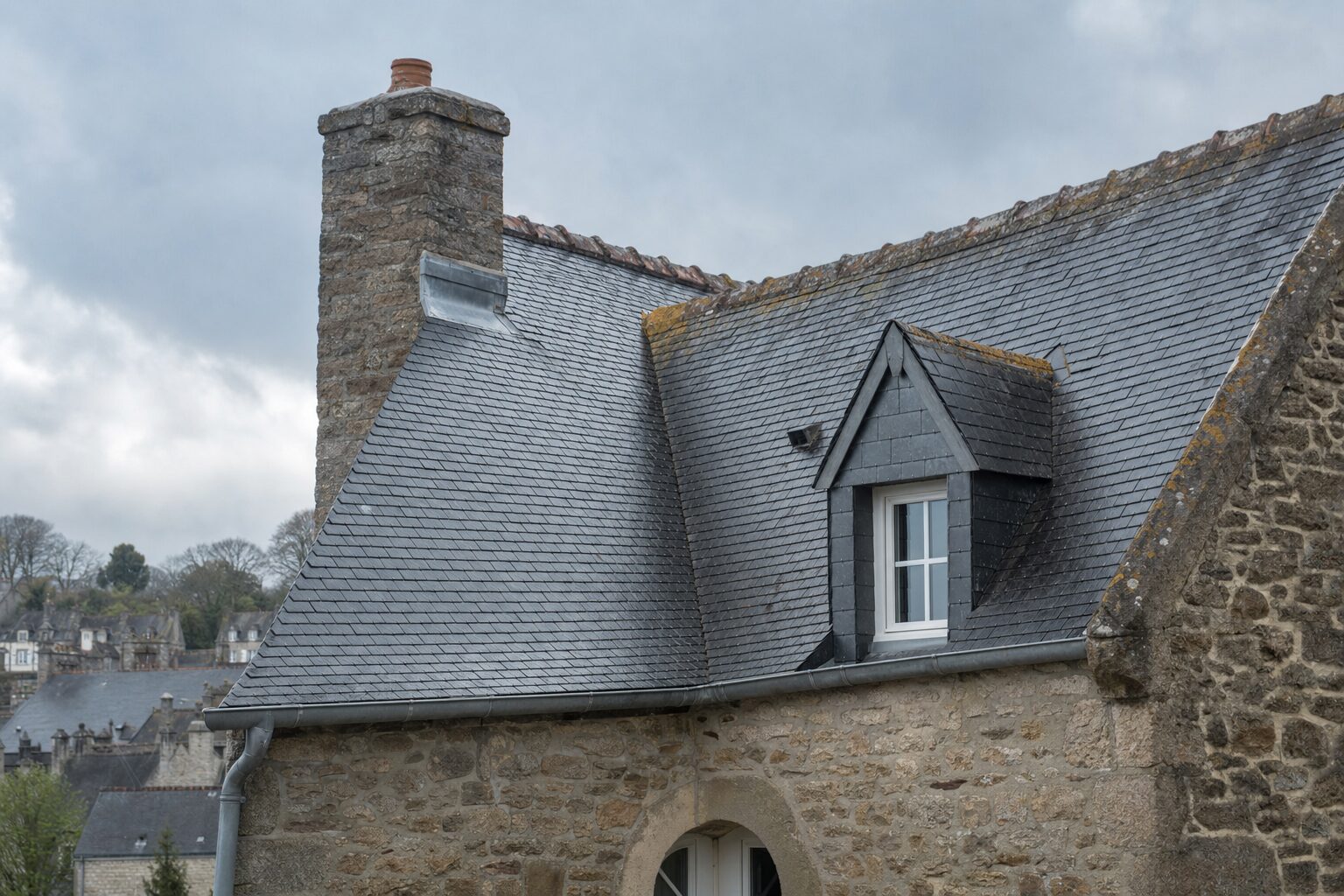 Toiture en ardoise naturelle d'une maison bretonne à Quimper, versants et souche de cheminée sous un ciel changeant